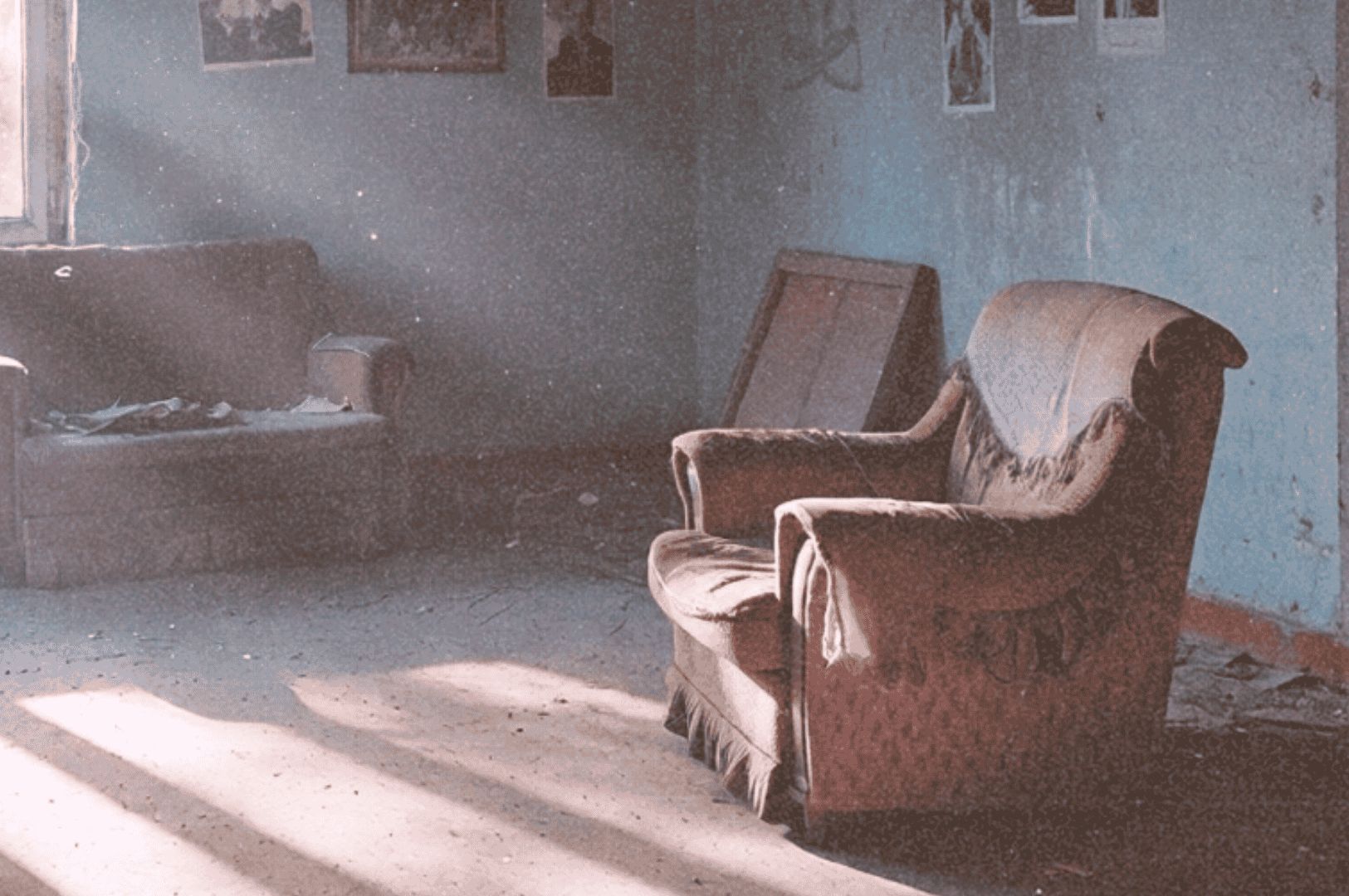 A decaying public housing room with tattered armchairs, peeling blue walls, and sunlight casting long shadows—evoking the quiet absence of its final residents.