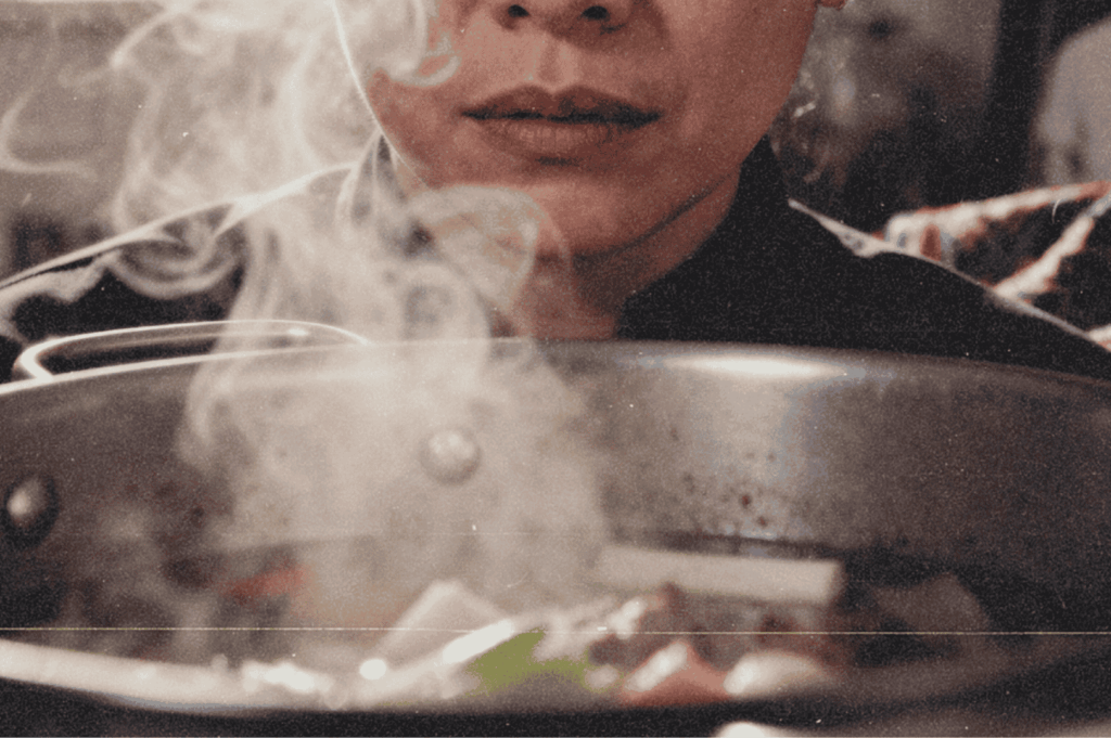 Close-up of a cook leaning over a steaming pot of soup with vegetables, capturing warmth and focus.