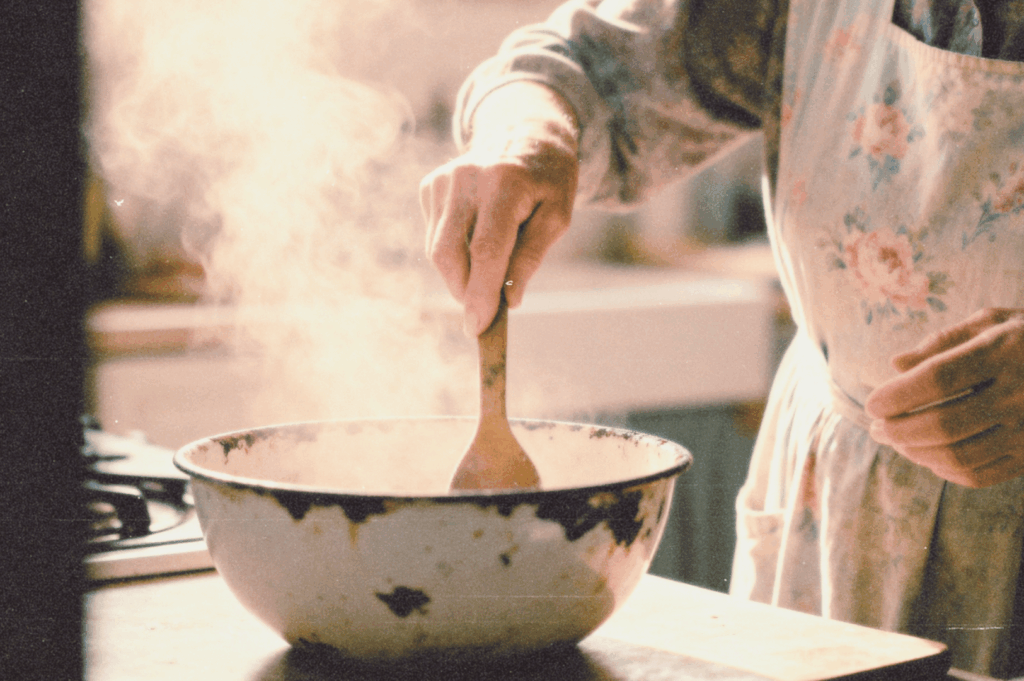 Close-up of an older person’s hands stirring a steaming bowl in a warm, well-worn kitchen, suggesting a treasured family recipe being prepared.