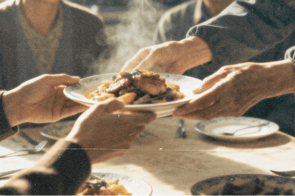  Hands passing a steaming home‑cooked dish at a family table, capturing care and tradition.