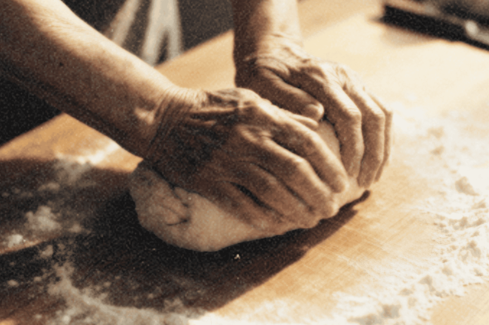 Hands kneading dough on a floured wooden table, warm kitchen light.