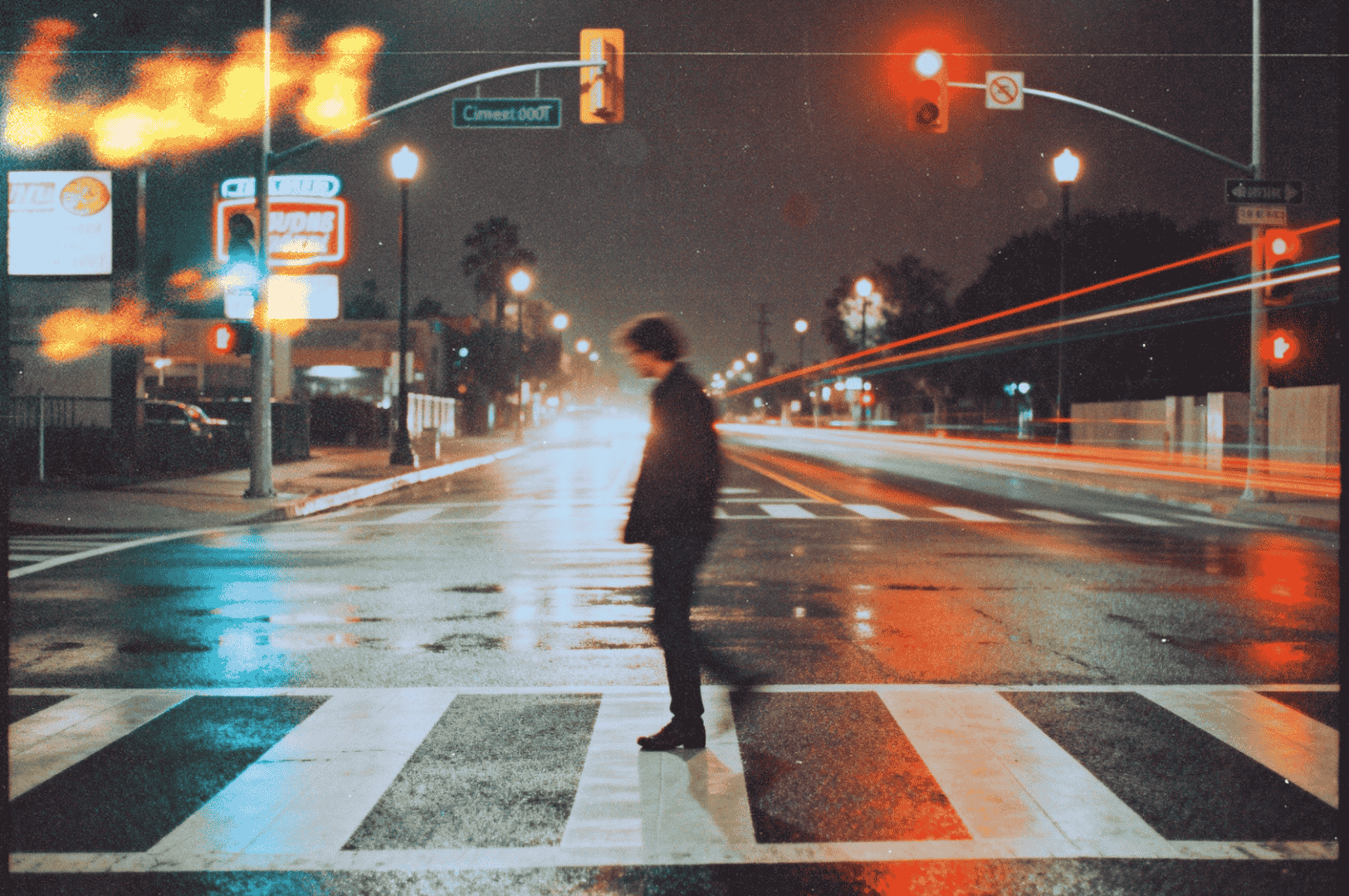 Person crossing a wet city street at night with blurred car lights and glowing traffic signals.