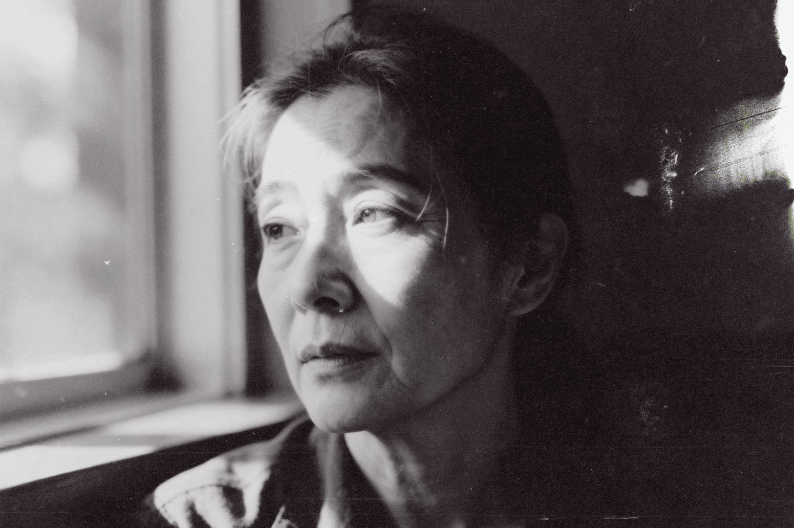 Close-up portrait in black and white of a person looking outside, thoughtful expression.