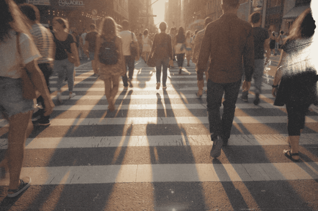 Golden-hour shadows stretch across a bustling city crosswalk as pedestrians flow in every direction—capturing the fleeting rhythm of urban life in motion.