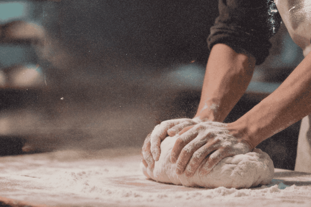 Hands kneading dough on a floured surface, capturing the tactile rhythm of night-shift baking in progress.