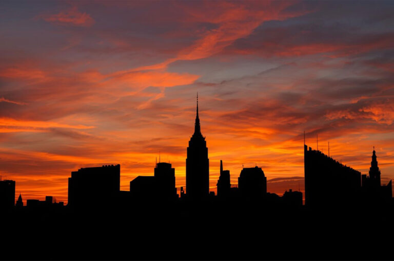 Silhouette of the New York City skyline featuring the Empire State Building against a dramatic, fiery orange and red sunset.