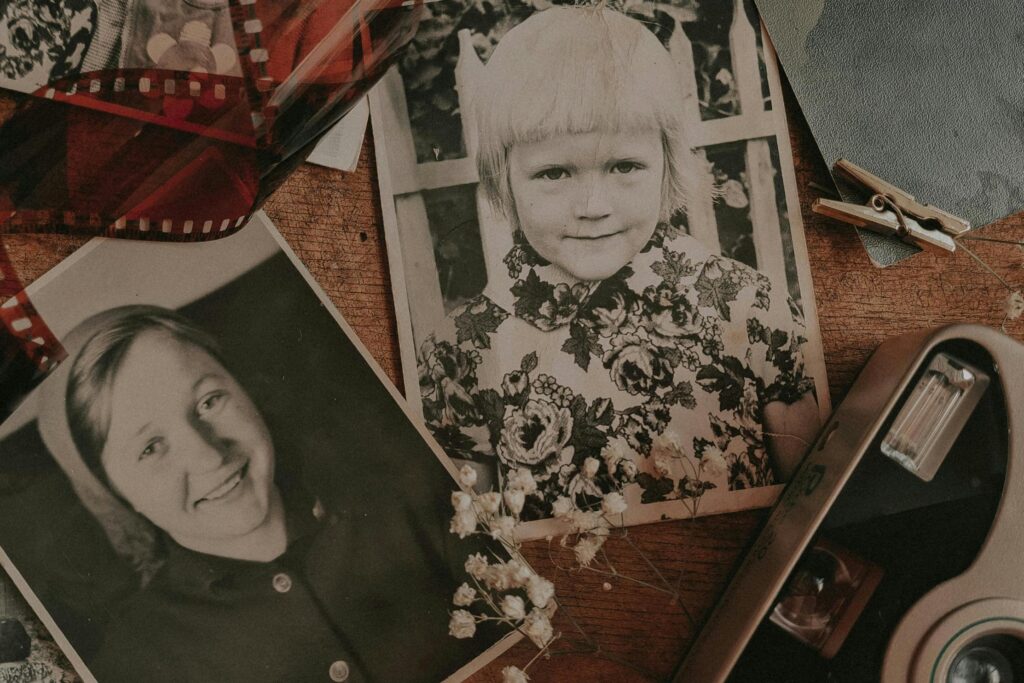 This nostalgic arrangement features scattered black-and-white snapshots on a wooden surface, highlighting a portrait of a young girl in a floral dress alongside a smiling woman.