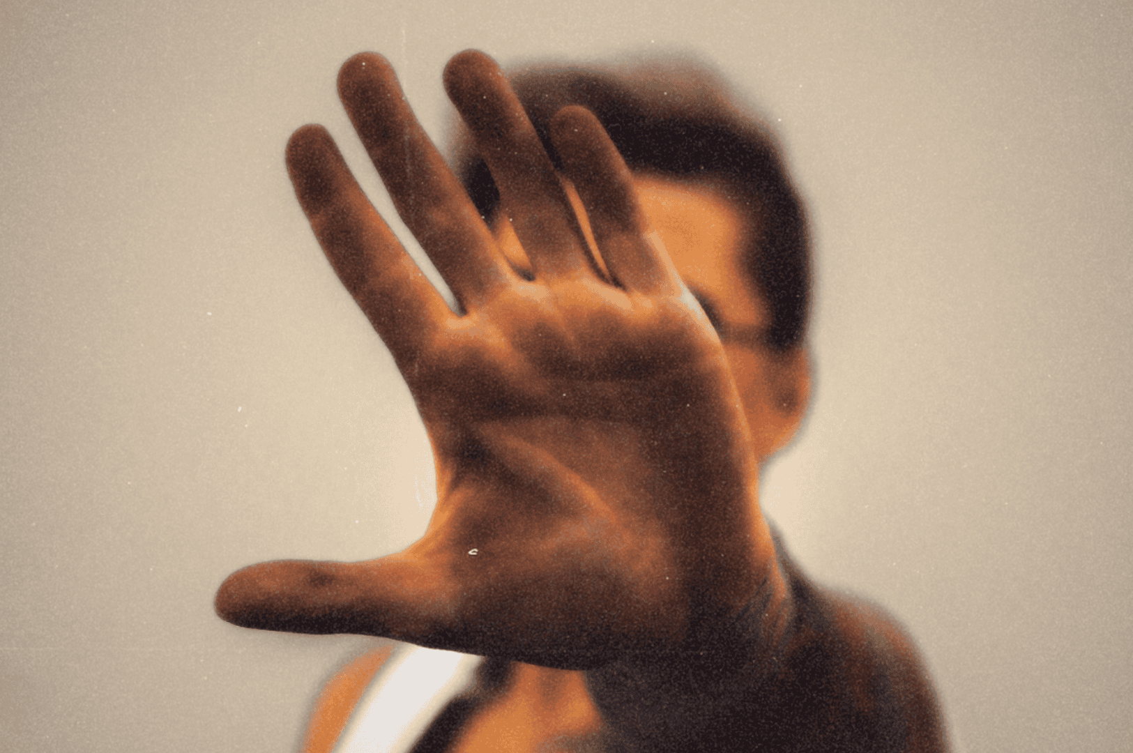 A sharply focused open hand blocks the camera, fingers splayed in quiet defiance, while the blurred figure behind it fades into anonymity—evoking the palm as both shield and storyteller.