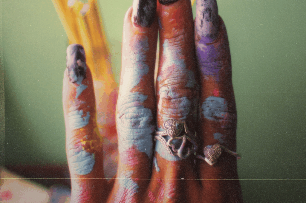 A close-up of a paint-splashed hand adorned with ornate rings, fingers pressed together in quiet ceremony—an intimate portrait of creativity worn like ritual.