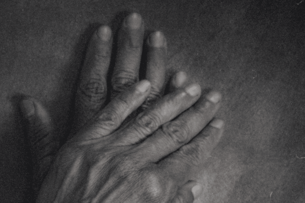 Two hands—one large, one small—rest gently atop each other in monochrome stillness, their aligned fingers quietly echoing trust, tenderness, and the silent bond of shared time.