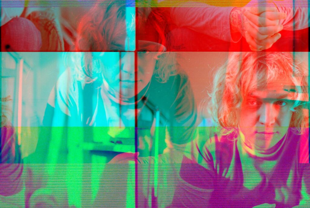  This portrait features a young man with curly hair whose image is fragmented by heavy digital glitch effects and sharp color separation.