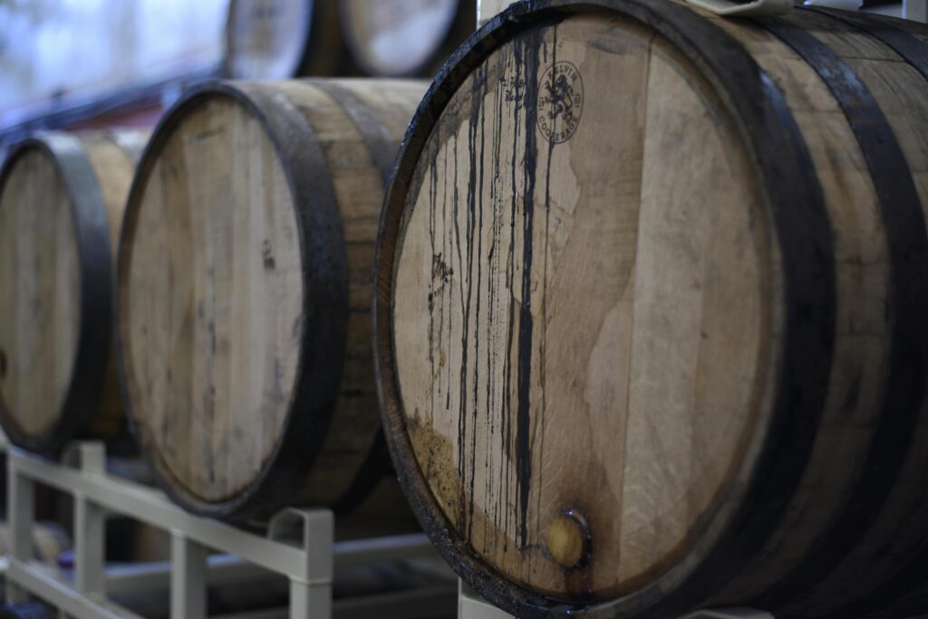 Several wooden barrels are lined up on metal racks, their curved faces stained with dark drips from aging liquid.