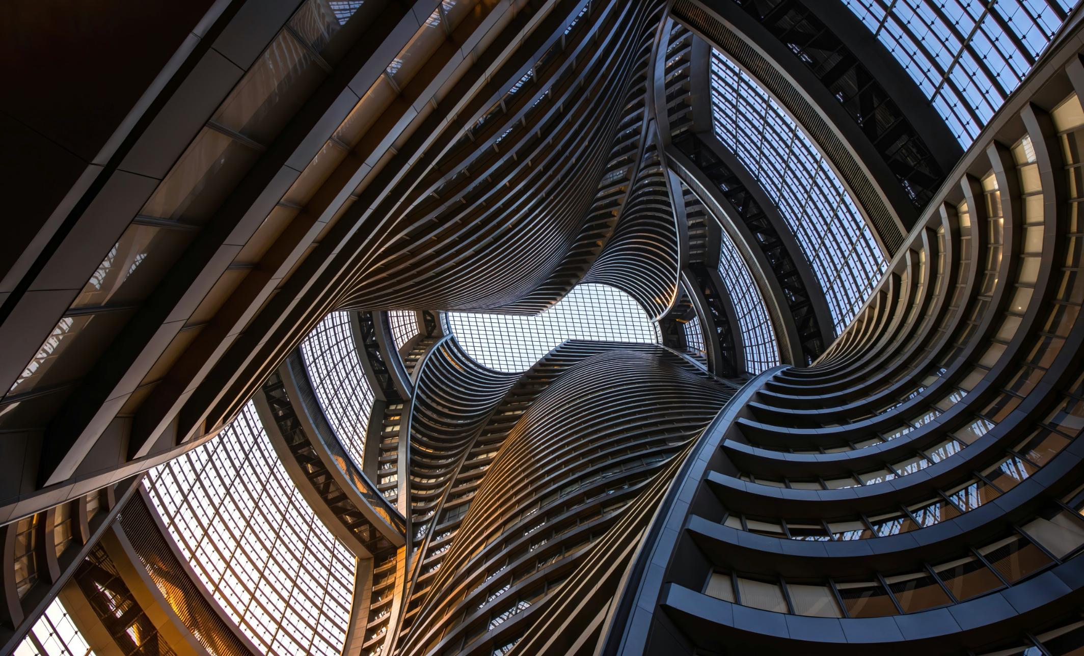 This architectural photograph captures a dizzying upward view of a futuristic atrium, featuring sweeping, organic curves of stacked balconies that spiral toward the center.