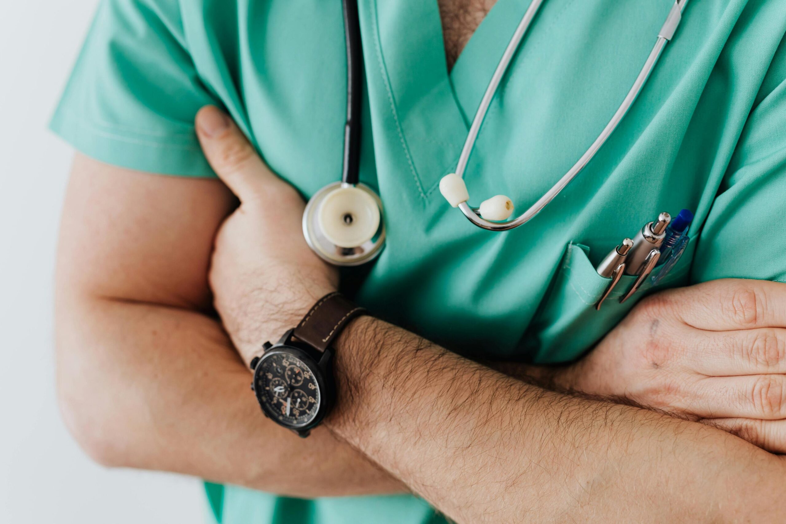 A healthcare professional wearing green scrubs stands with their arms firmly crossed over their chest.