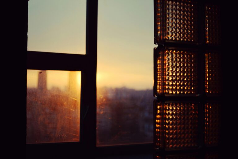 Warm sunset light filters through a window, casting a golden glow over a city skyline in the distance.