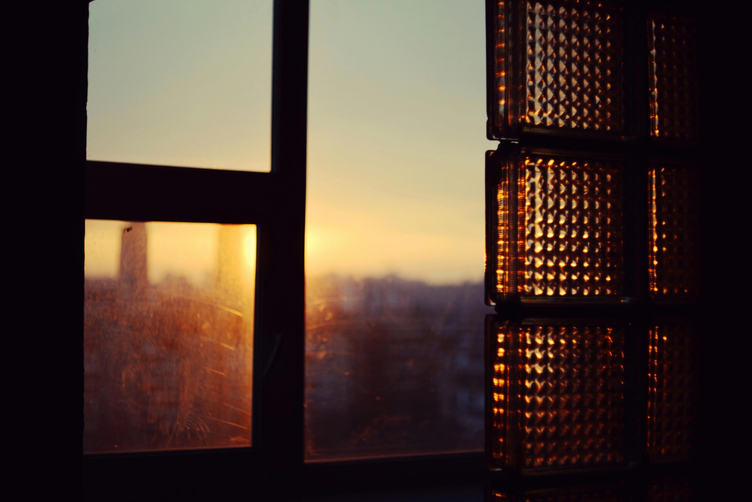 Warm sunset light filters through a window, casting a golden glow over a city skyline in the distance.