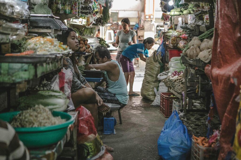 This image captures the busy atmosphere of an indoor market, where vendors are surrounded by overflowing crates and shelves of fresh produce.