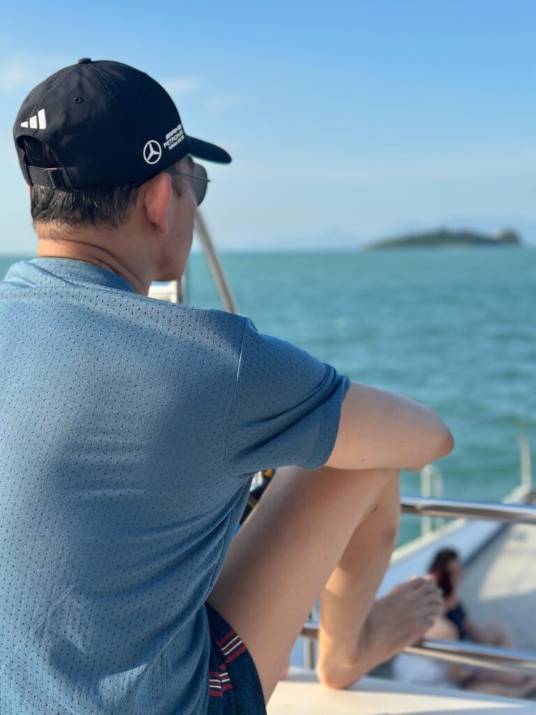 A close-up, over-the-shoulder shot of a man wearing a blue perforated polo shirt and a black Mercedes-AMG Petronas baseball cap.