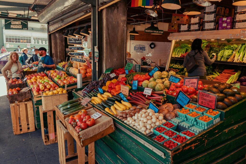 This vibrant outdoor market features a wide array of fresh produce, including neatly arranged fruits, vegetables, and mushrooms labeled with handwritten price signs.