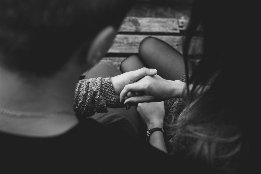 This black and white photograph captures an intimate moment from an over-the-shoulder perspective of a couple holding hands while sitting together.