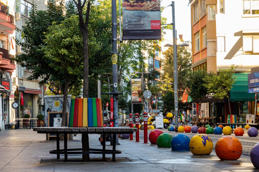 This vibrant city street features a series of colorful, spherical bollards lining the edge of a pedestrian walkway next to multi-story buildings.