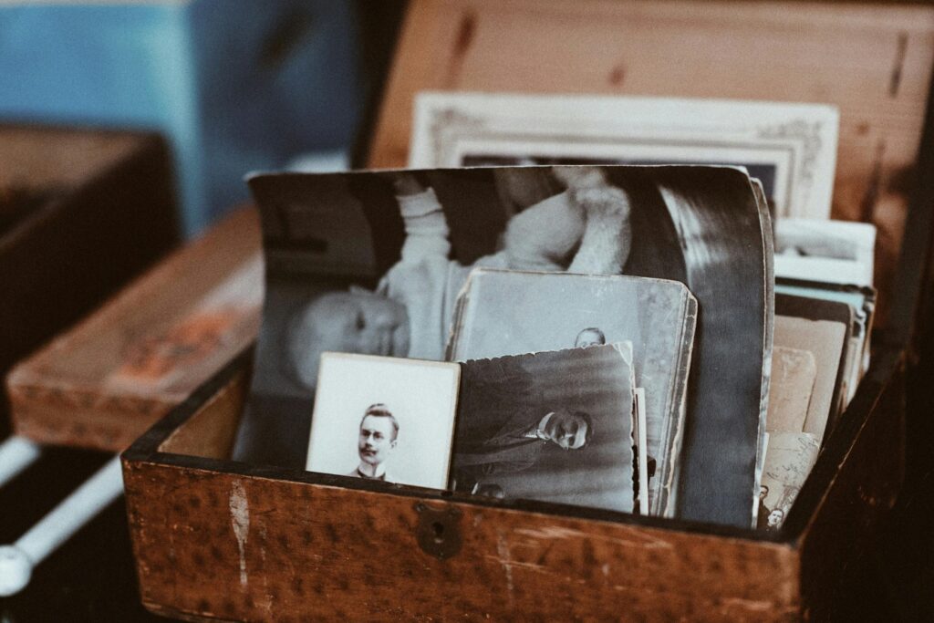 A collection of vintage black-and-white photographs is tucked inside an aged, textured wooden box with a small keyhole. The images feature portraits of people and a baby, evoking a sense of nostalgic history and forgotten memories.