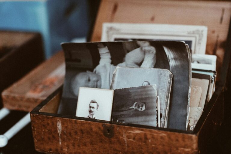 A collection of vintage black-and-white photographs is tucked inside an aged, textured wooden box with a small keyhole. The images feature portraits of people and a baby, evoking a sense of nostalgic history and forgotten memories.