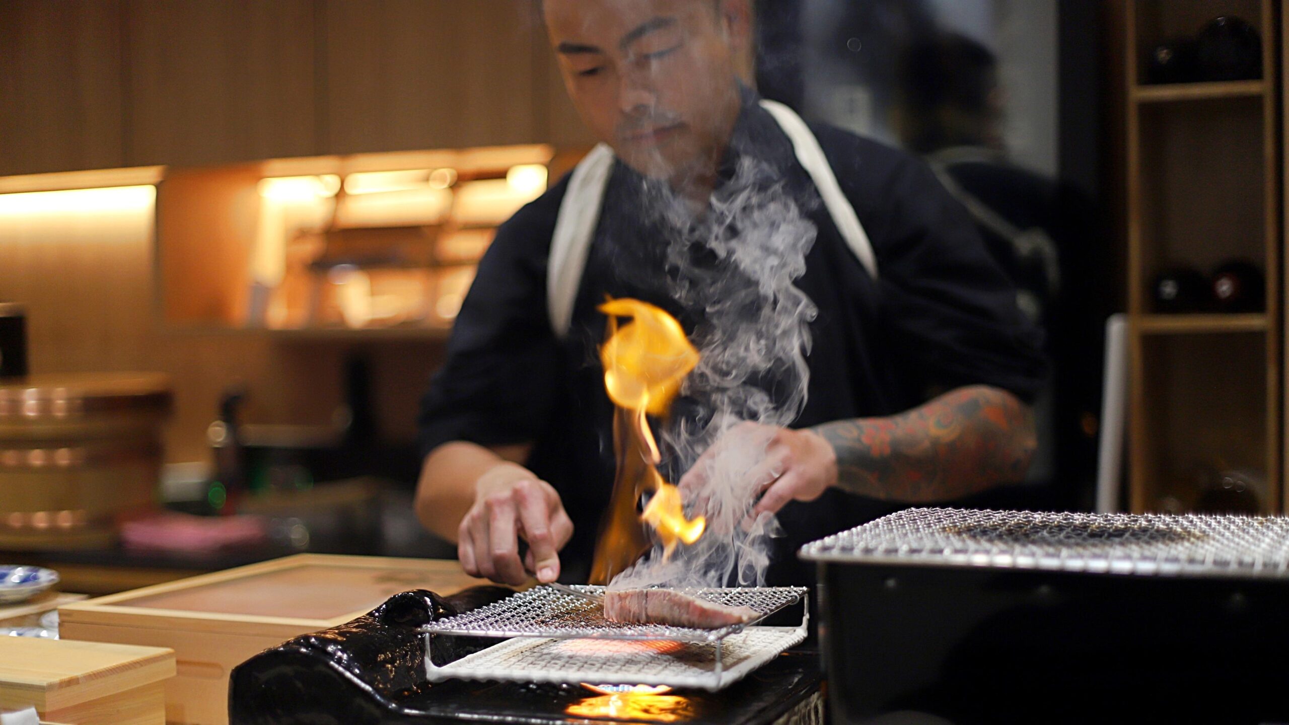Sushi Masa using the cooking style of Aburi on a wagyu beef as the flames and smoke rise above the meat as the chef meticulously cook it.