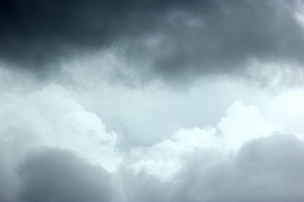 Heavy, dark storm clouds hang over a layer of bright, billowy white clouds. The stark contrast creates a dramatic and moody atmosphere across the entire frame.