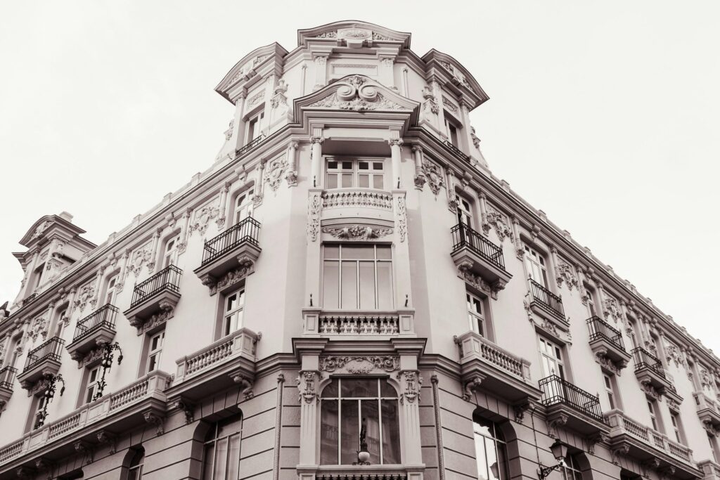 This stately, multi-story building showcases a light-colored facade adorned with elaborate Neoclassical carvings and numerous balconies.
