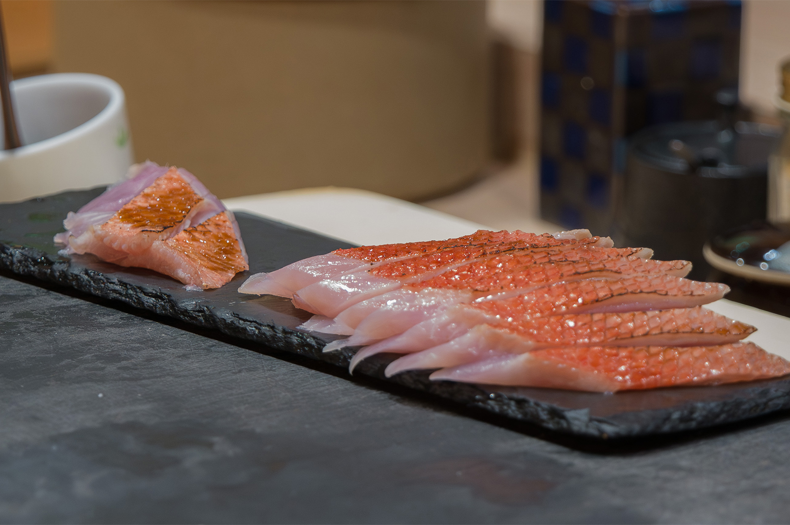 Slices of Kinmedai (Splendid Alfonsino) sashimi with seared skin served on a black stone plate at Sushi Masa by Ki-setsu.