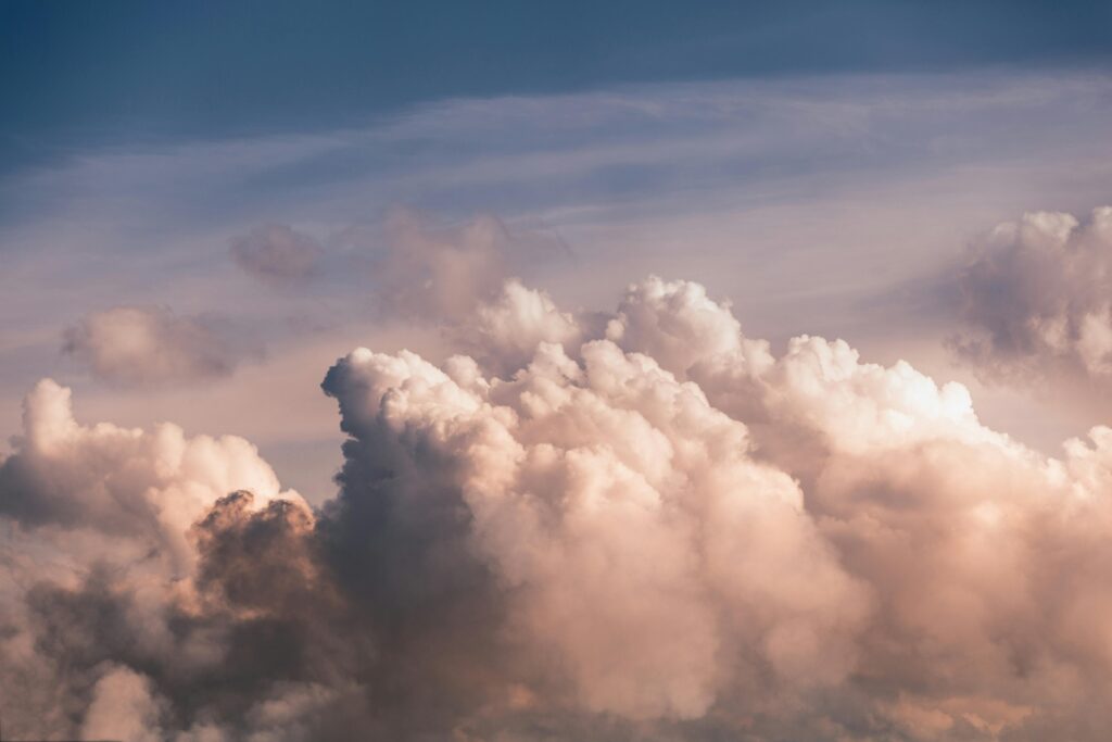 A thick bank of cumulus clouds rises toward the center of the frame, illuminated by a warm, golden glow that suggests a sunset or sunrise. Above the billowing white peaks, the sky transitions into a soft, hazy blue with thin streaks of wispy clouds.
