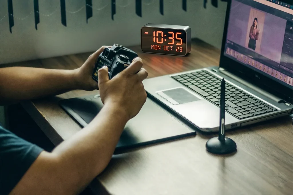Photographer editing images at a desk with a DSLR camera, laptop, and graphics tablet.