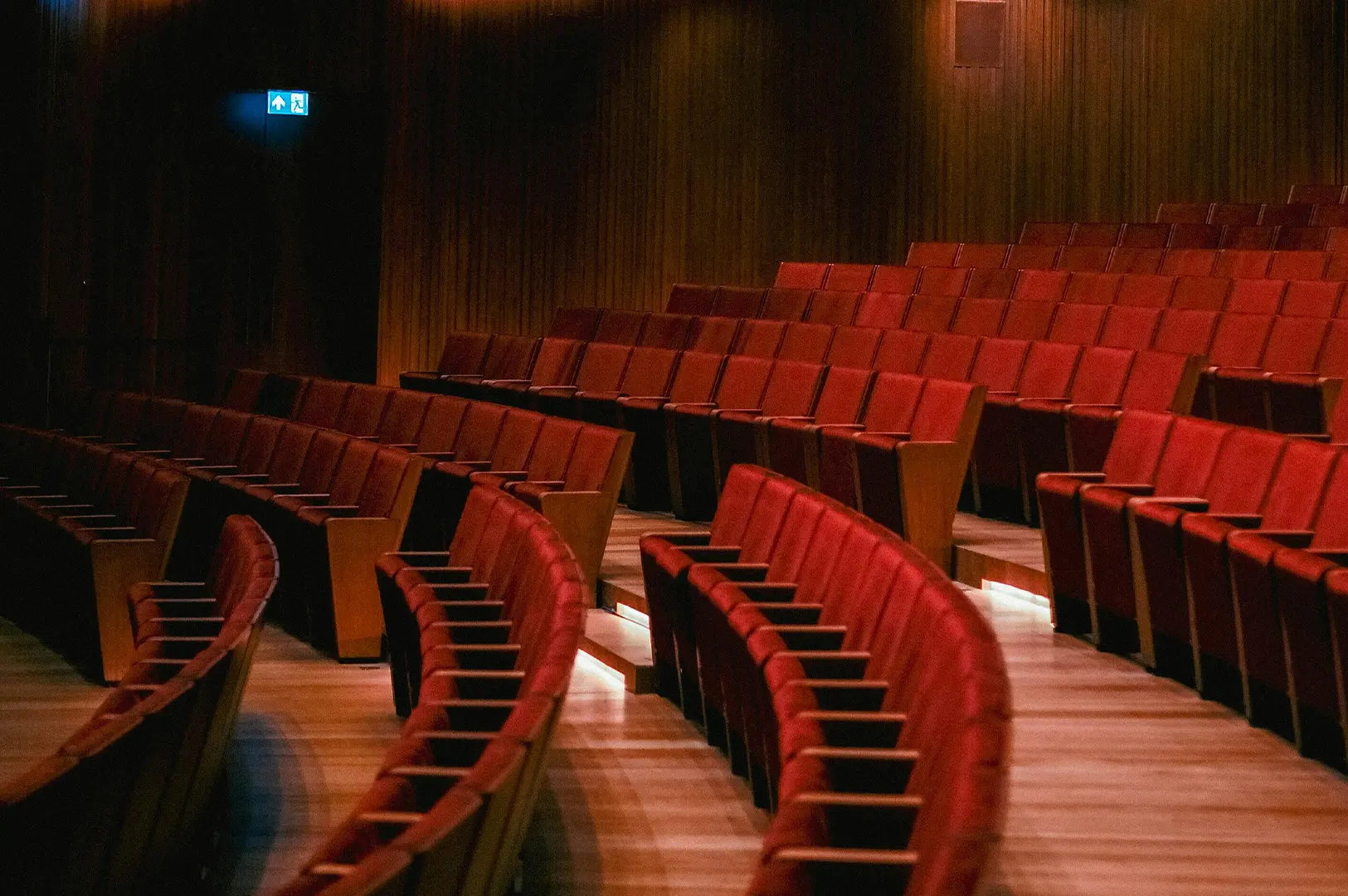 Empty theater rows with red velvet seats and wood paneled walls.
