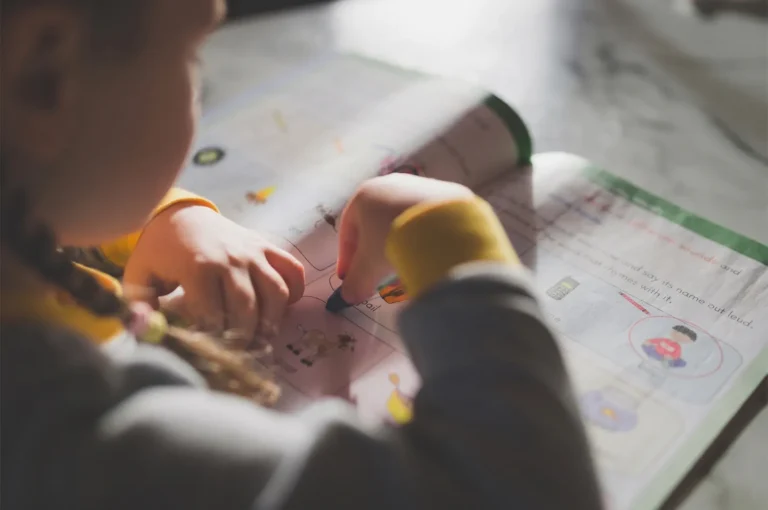 Young girl with braided hair using a crayon to complete an educational workbook activity.