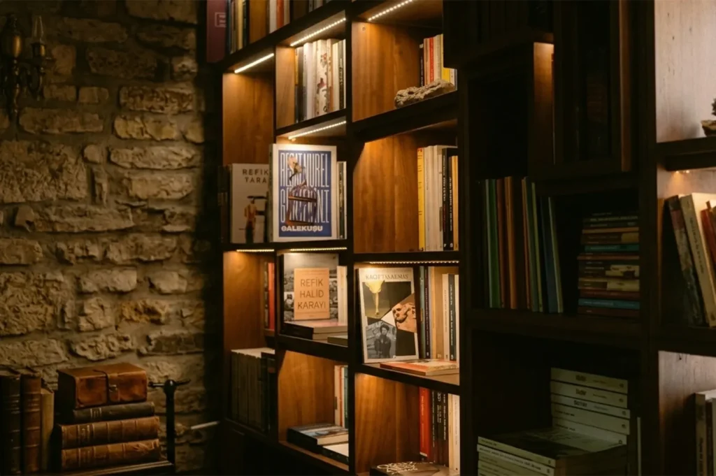 Modern wooden bookshelf with integrated LED lighting against a rustic stone wall.