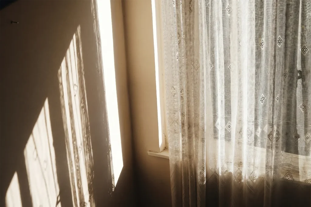 Warm afternoon sunlight casting patterned shadows through a lace curtain onto an interior wall.