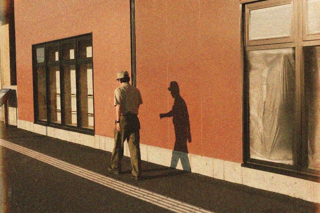 Man in uniform walking past a modern orange building, casting a long shadow on the wall during golden hour.