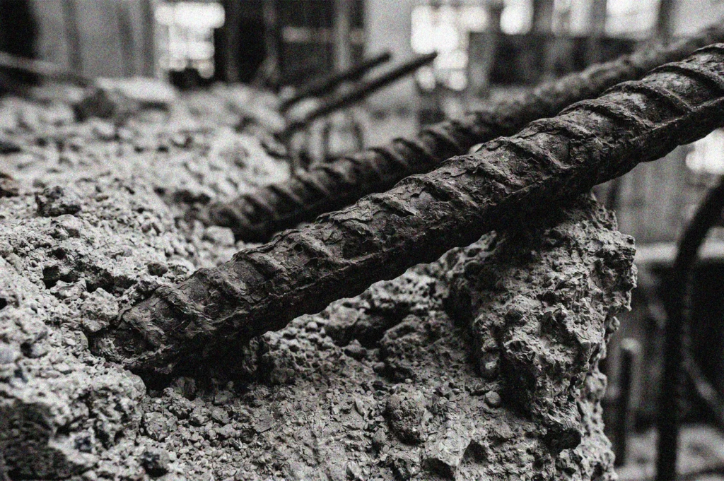 Close-up black and white photograph of rusted steel rebar embedded in rough, broken concrete rubble at a construction site.