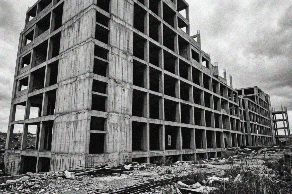 Black and white photograph of an abandoned concrete building skeleton at a brutalist construction site under a cloudy sky.