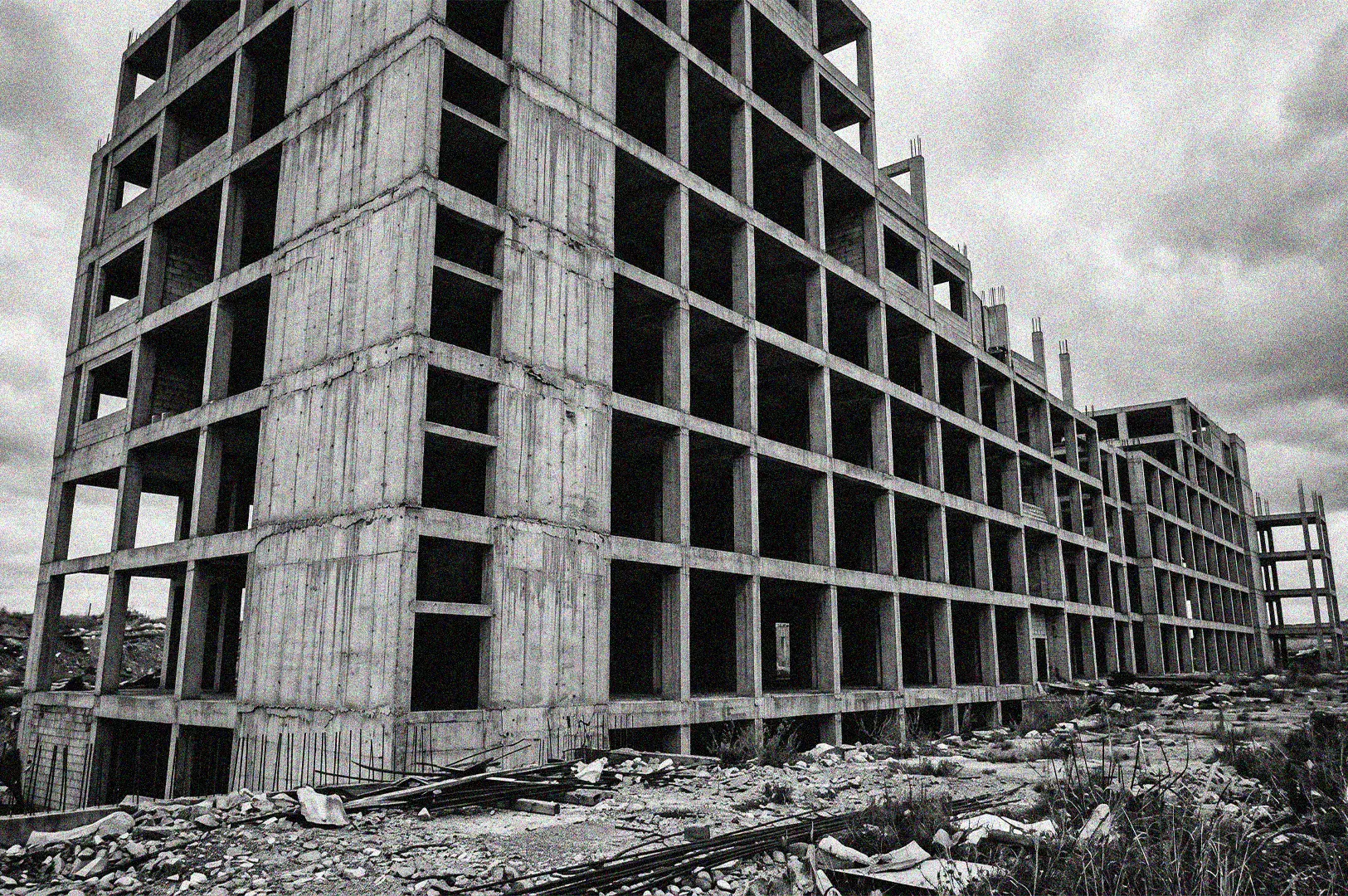Black and white photograph of an abandoned concrete building skeleton at a brutalist construction site under a cloudy sky.