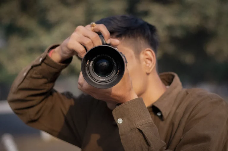 Photographer holding a DSLR camera and taking photos outdoors with a blurred natural background and shallow depth of field.