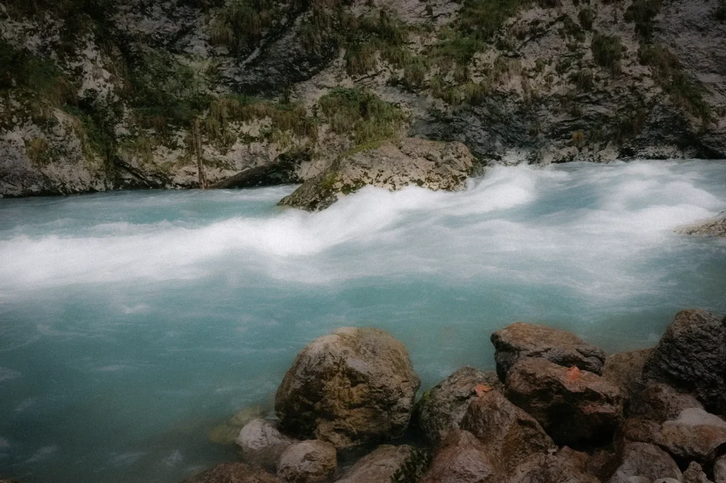 Fast-flowing glacial spring water rushing through rocky river rapids, surrounded by rugged stone formations in a pristine mountain landscape.