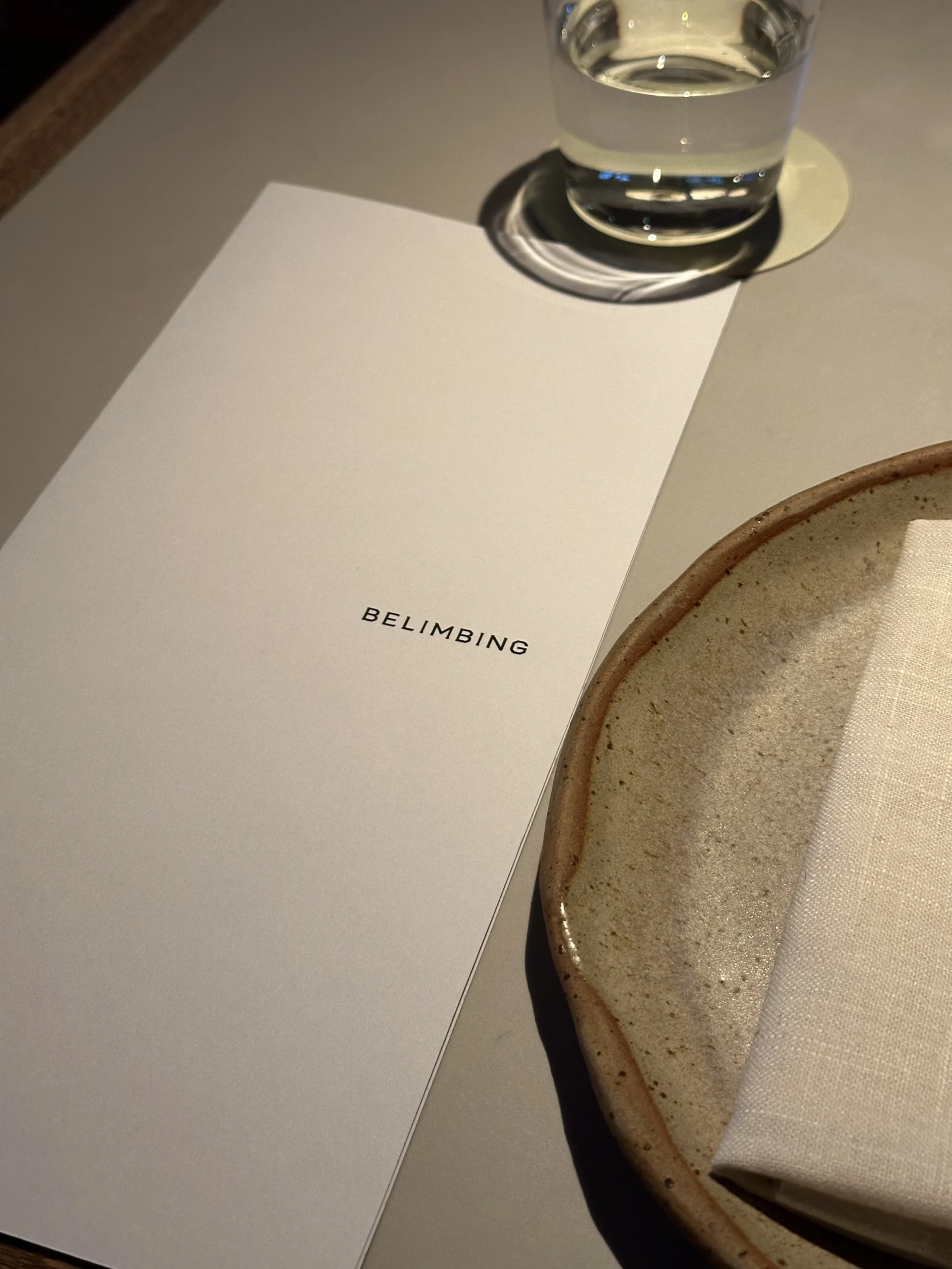 Belimbing restaurant menu on a dining table next to a plate and water glass.