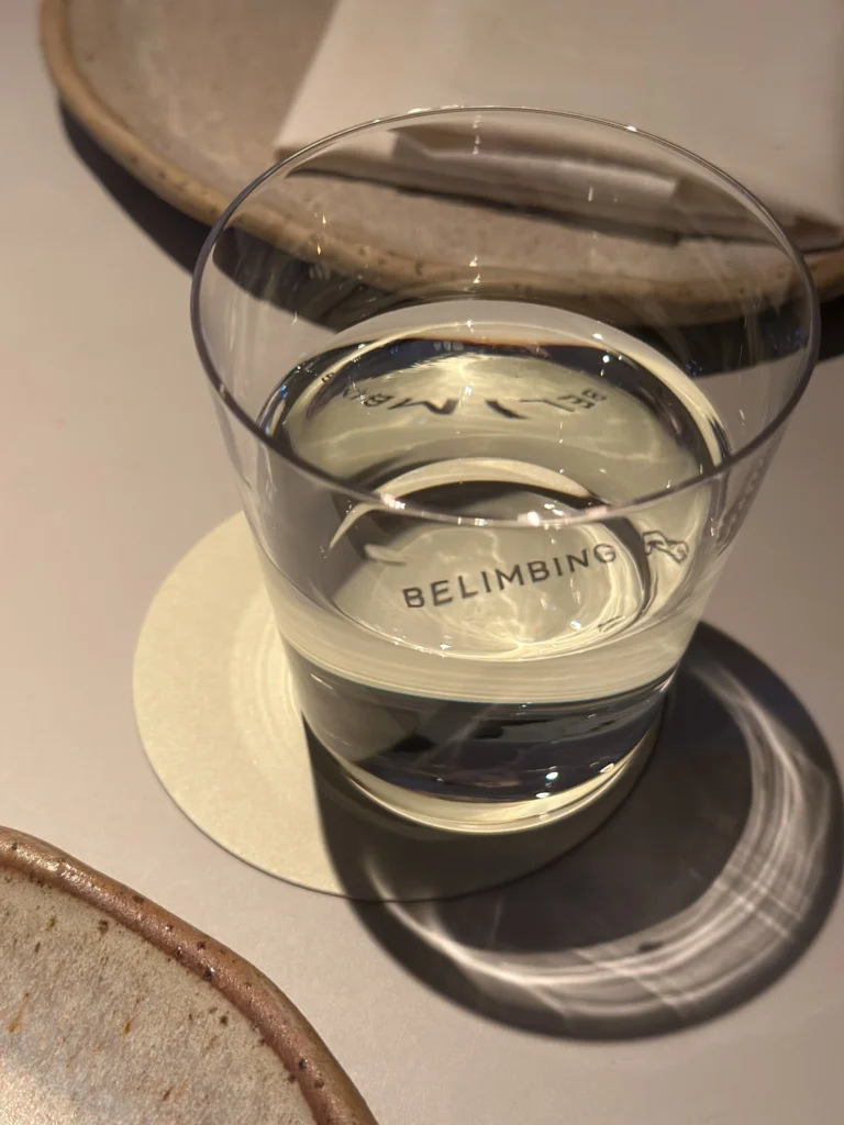Glass of water reflecting the Belimbing restaurant logo on a coaster.
