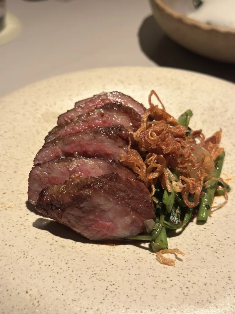 Sliced medium-rare wagyu steak with crispy shallots and greens at Belimbing restaurant.