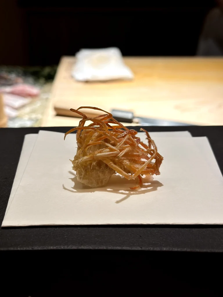 Crispy fried burdock root tempura served in a delicate nest-like presentation at a Japanese omakase counter.