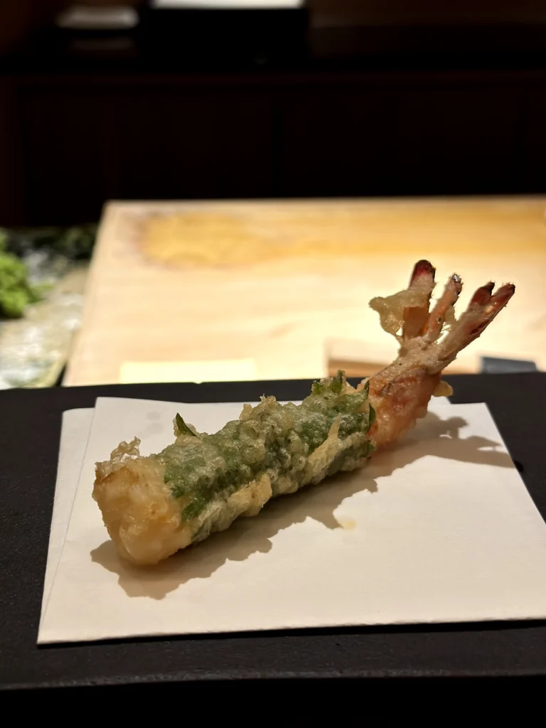 Tiger prawn wrapped with shiso leaf tempura featuring a crisp batter and vibrant green herb coating.