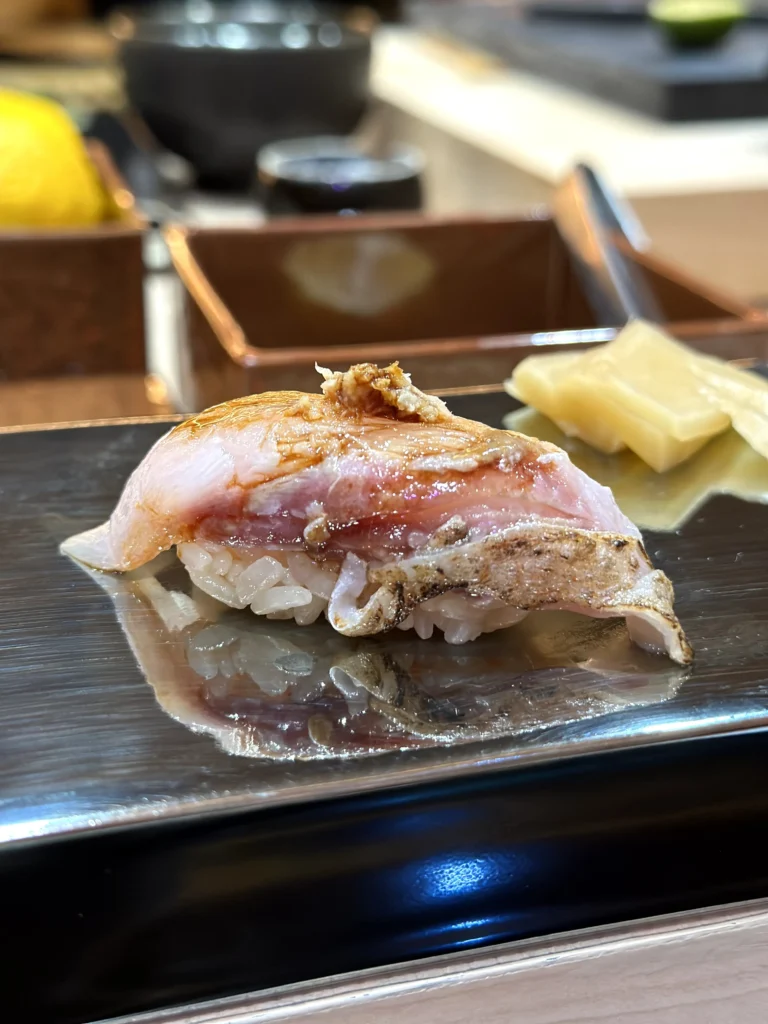 Seared fish nigiri sushi with lightly charred skin served on a metal sushi plate at a Japanese restaurant