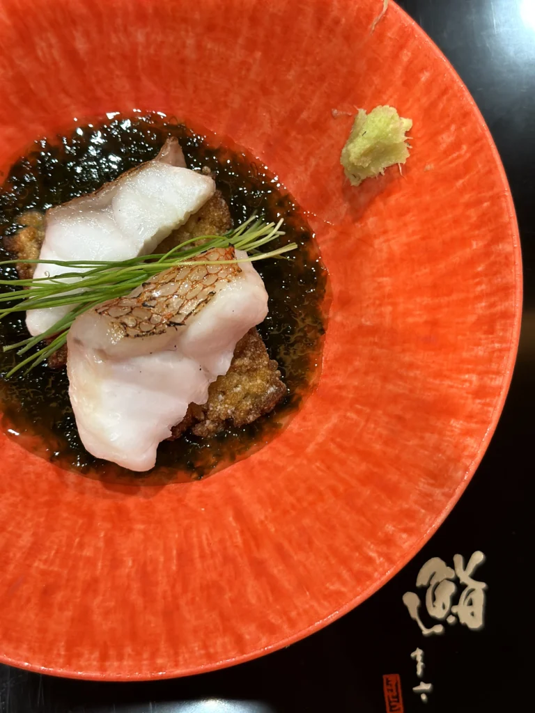 White fish served over crispy fried base with seaweed sauce and wasabi in a vibrant red bowl